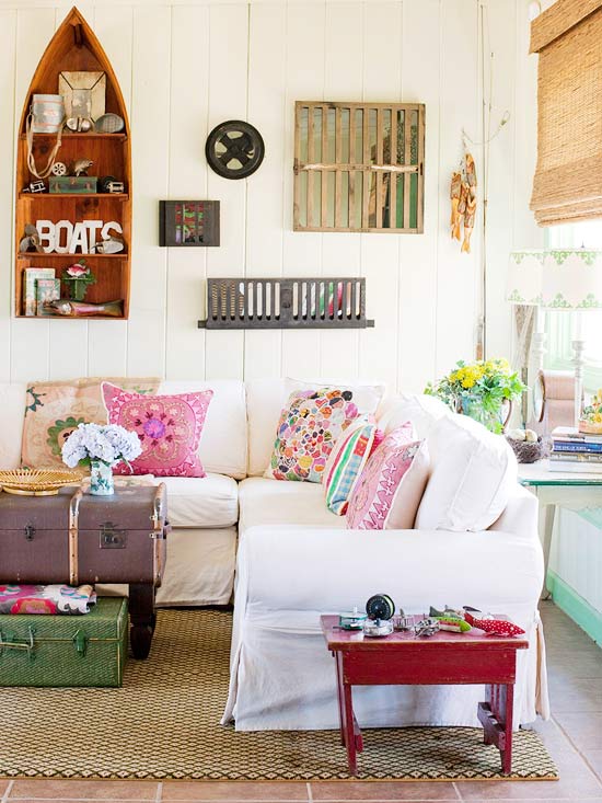 A white sectional couch with multicoloured pillows and a suitcase vintage table in the middle of the room.