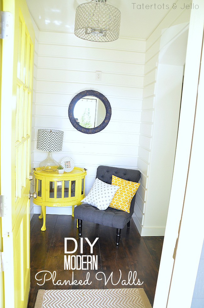 Walls that are planked with a yellow table and grey chair by the wall with yellow and white pillows on the chair.