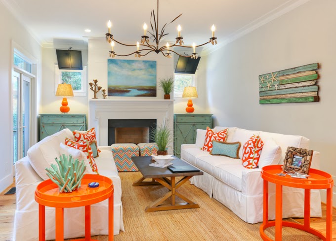 White couches, orange side tables and a beachy chandelier.