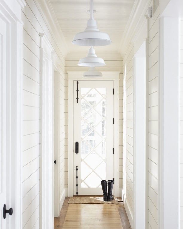 An all white panelled hallway with a pair of black boots by the front door.