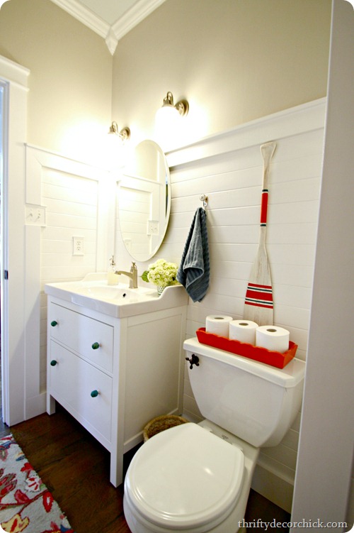 A small bathroom with a white vanity, a red and white paddle on the wall.