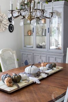 A wooden table with a chandelier above it and a small pumpkin centerpiece.