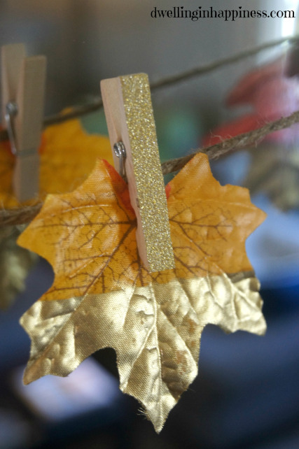 A leaf dipped in gold hanging by a sparkly gold wooden pin.