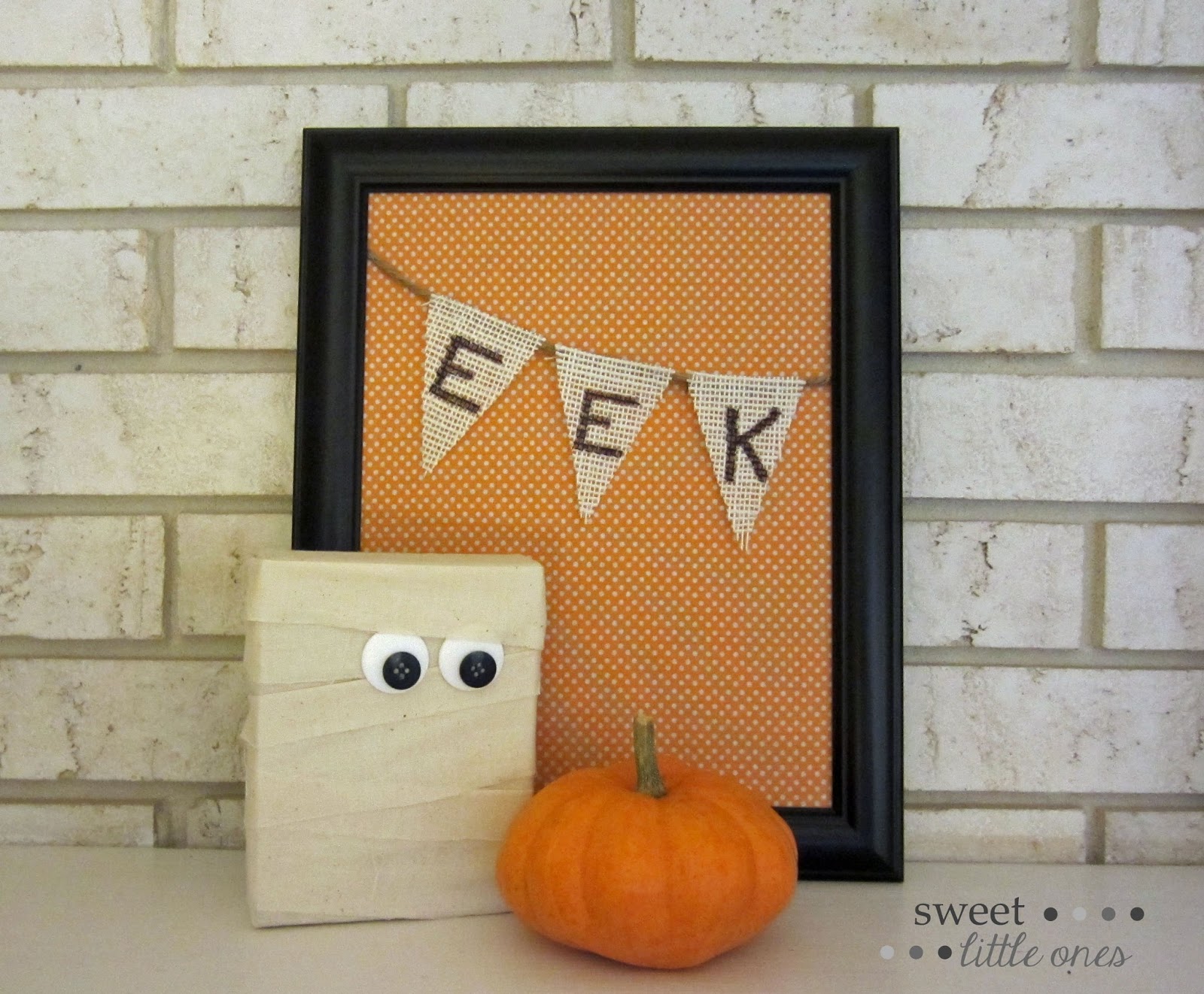 Eek sign in a picture frame beside a small pumpkin and a mummy.