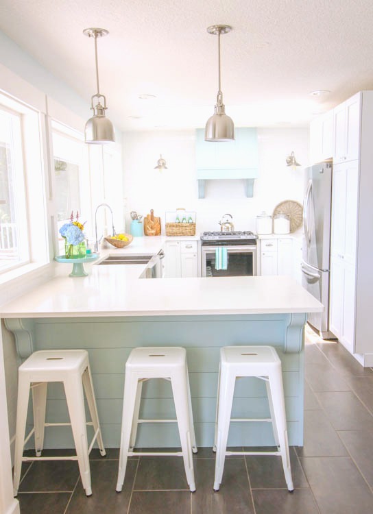 A white kitchen with light blue island and pendant hanging lights above it.
