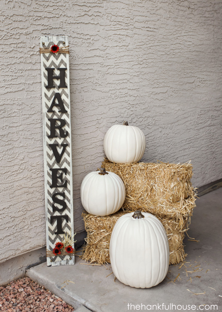 A harvest sign on the porch beside white pumpkins and bales of hay.