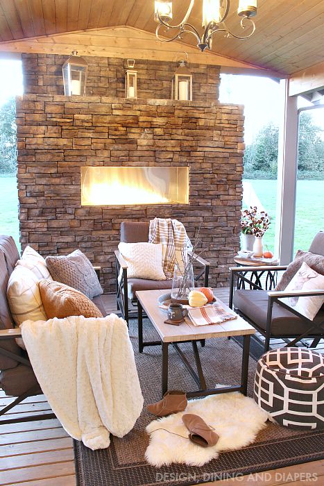 An outdoor fireplace with a brown and white pouf.   There is seats with blankets and faux fur.