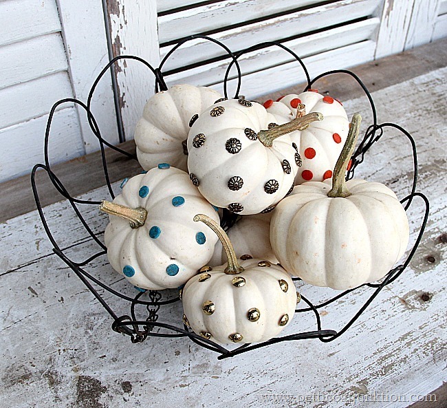 Small white decorated pumpkins in a wire basket on the front porch.