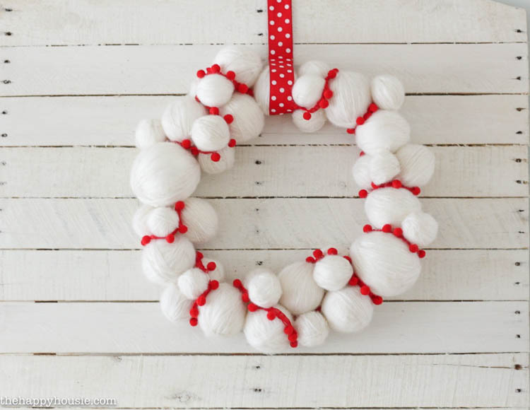Adorable quick and easy Yarn Snowball DIY Christmas Wreath hanging on the planked wall.
