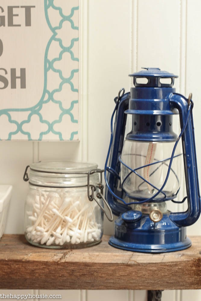 A navy blue lamp is on the shelf beside q tips in a jar.