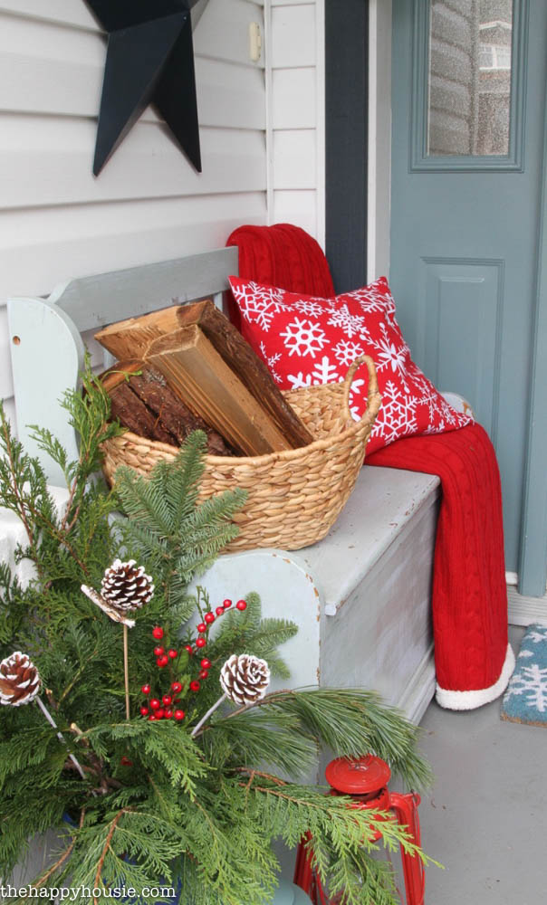 A red throw pillow and a red blanket is on the front porch bench.