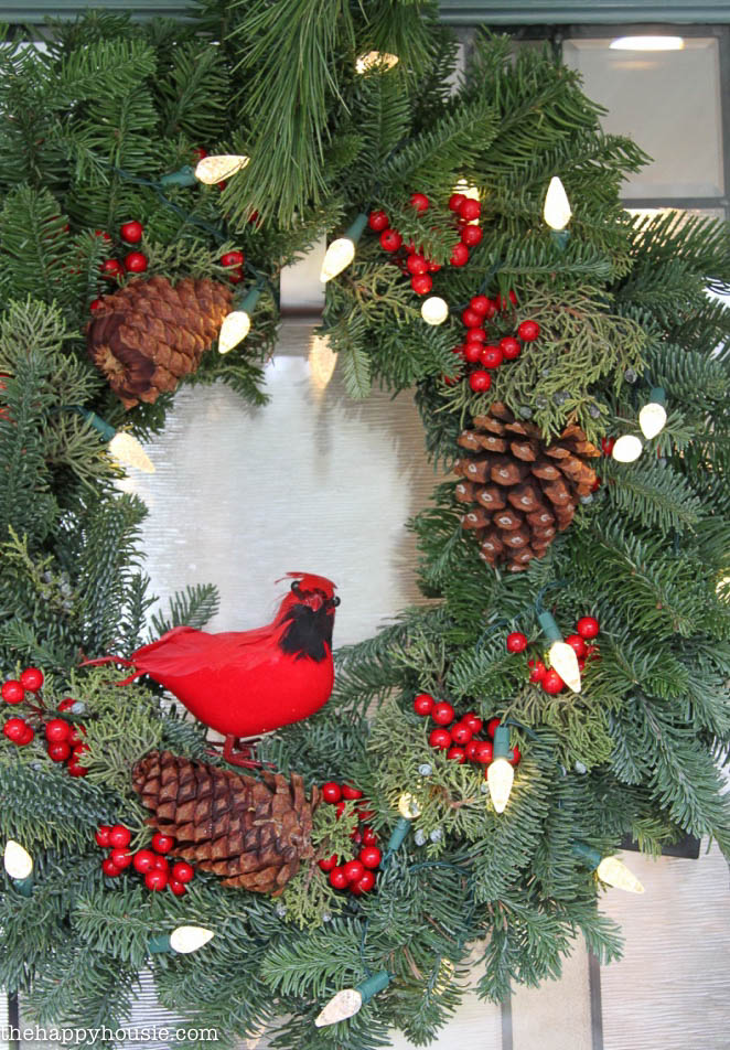 The Christmas wreath has a small red bird, berries, pinecones, and lights.