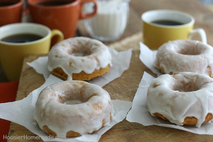 Easy Homemade Pumpkin Doughnuts sitting on a wooden cutting board with cups of coffee beside them.