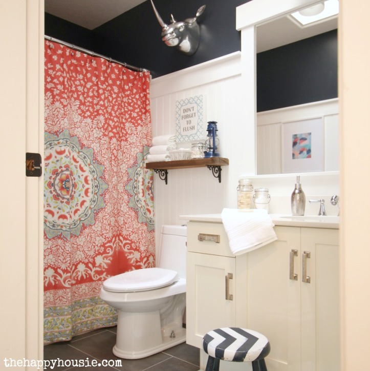 The main bathroom with a rhino head in silver on the wall, a small wooden shelf and a bright shower curtain.