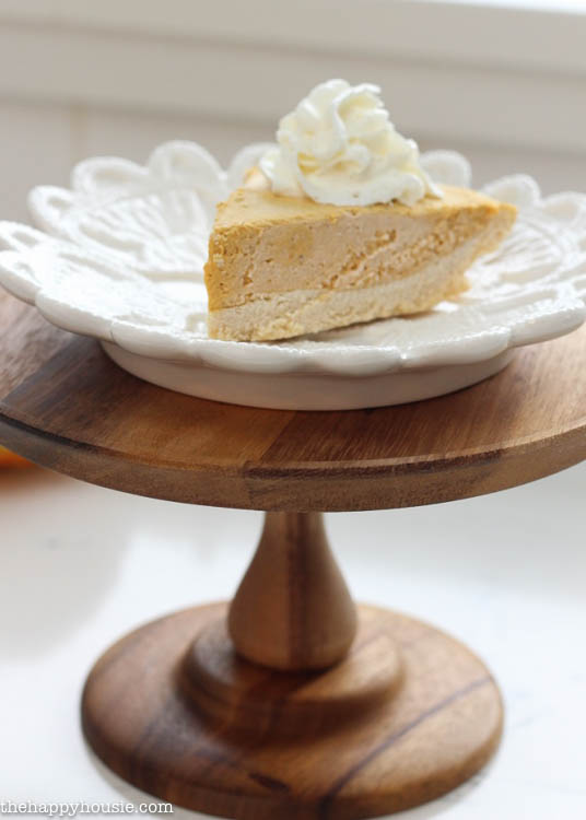 The pie on a white plate that is on a wooden cake stand