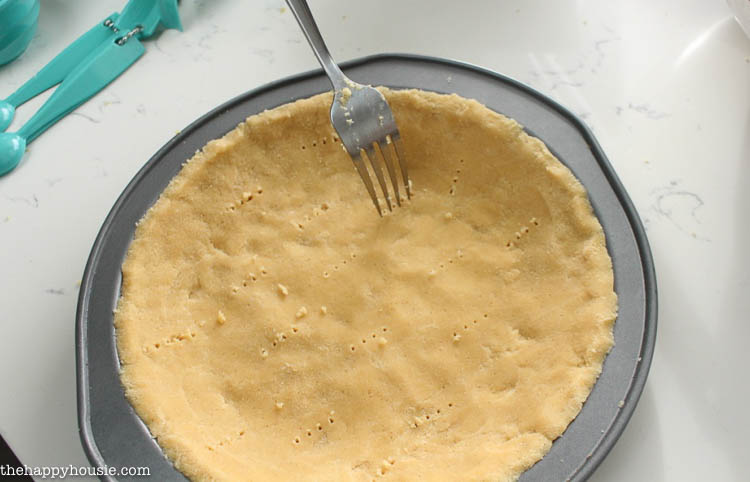The crust in a pie tin poking holes in it for baking.