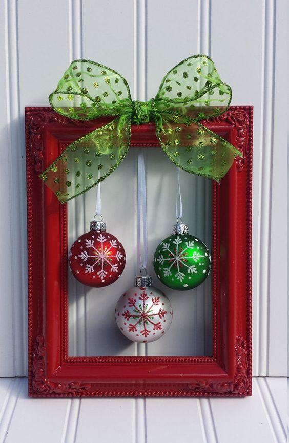 A red picture frame with Christmas ornaments hanging from it and a large green bow.