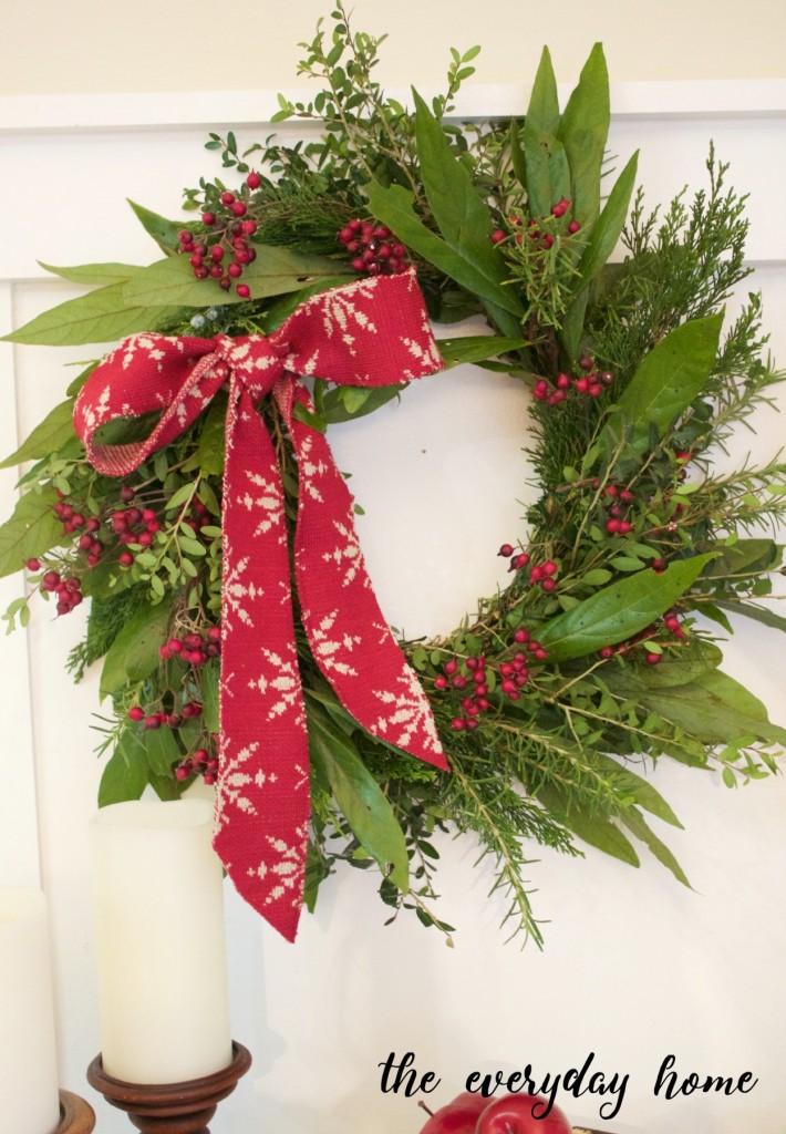 An evergreen wreath with a red and white bow, and red berries and greenery.