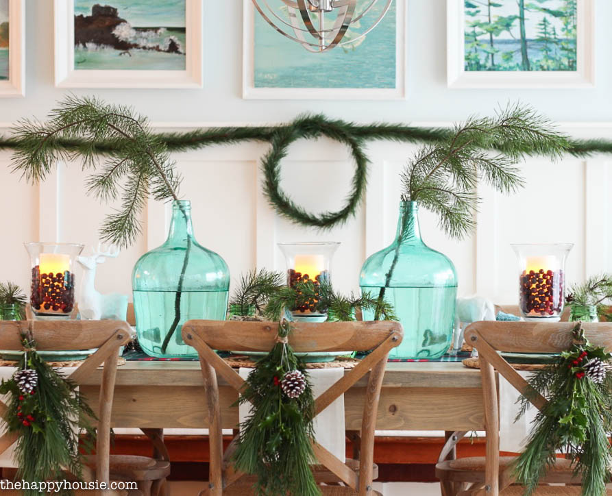 Evergreen branches with a painted pine cone are tied to the back of the wooden dining room chairs.