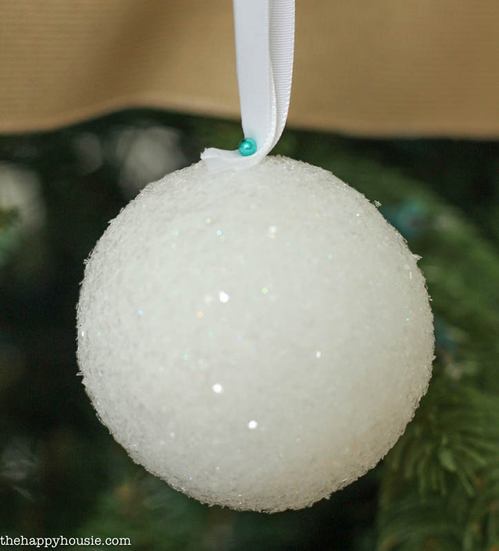 Using a push pin to attach the white ribbon to the styrofoam ball.