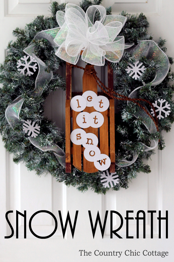A wreath with evergreen and flakes of snow.   There is a large white bow and a let it snow sign.