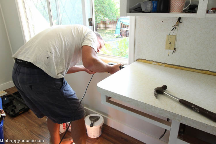 A man using a power tool in the kitchen to demo the counters.