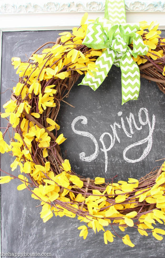 The yellow wreath hanging on a chalkboard with the word spring written on the board.