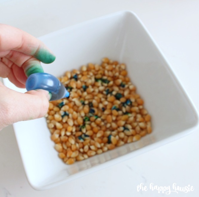 Adding dye to a bowl of unpopped popcorn.