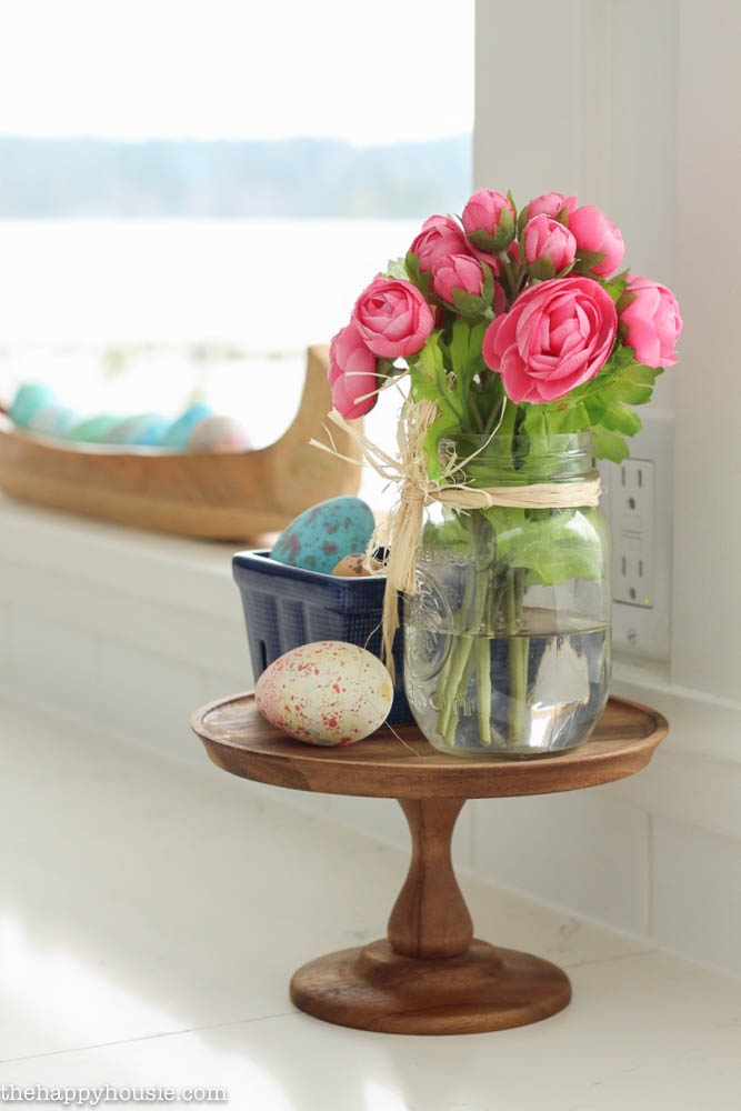 A jar filled with pink flowers is on a small cake stand.