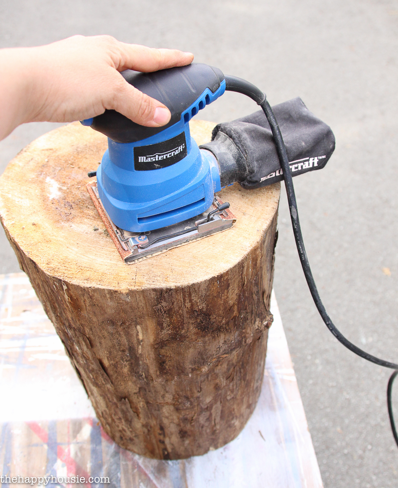 Using a palm sander to smooth the top of the tree stump.