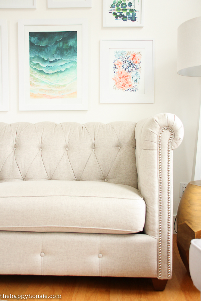 A light coloured sofa that is tufted in the living room with art pictures above it.