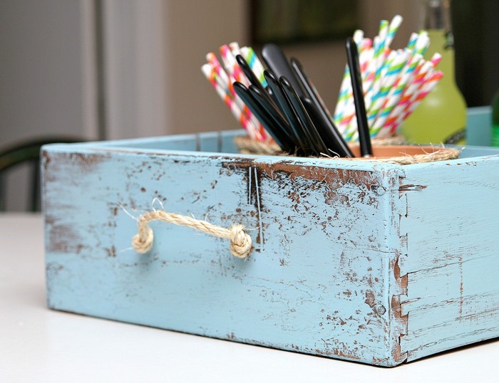 A distressed blue wooden drawer with cutlery inside it.