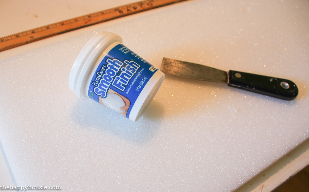A putty knife and a plastic container of Smooth Finish on the table.