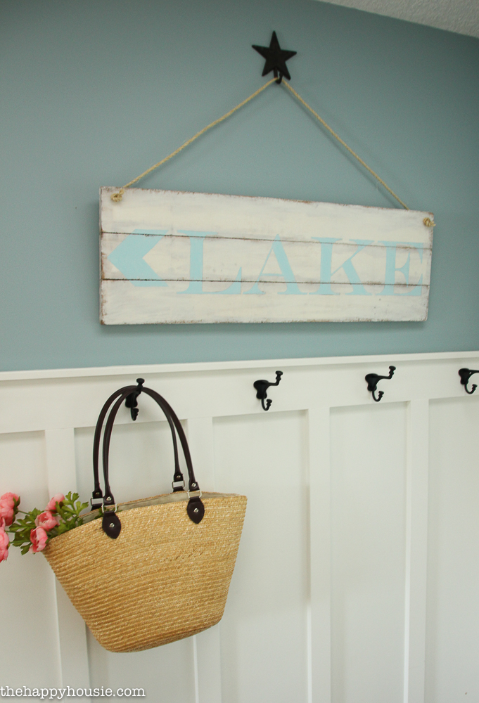 The sign above the coat hooks with a basket purse with flowers in it hanging on a hook.