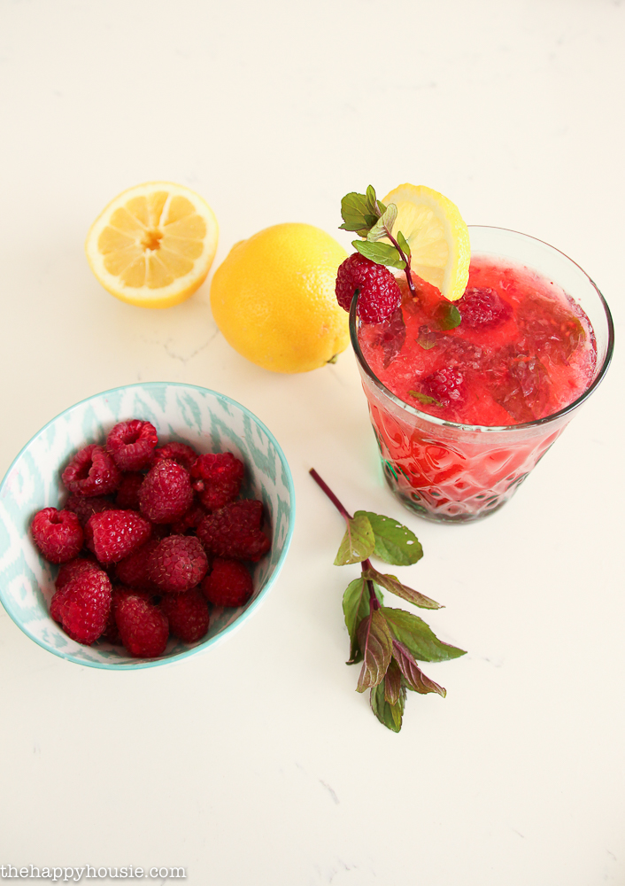 The raspberry lemonade in a glass with a slice of lemon and a raspberry on the rim and a sprig of mint.