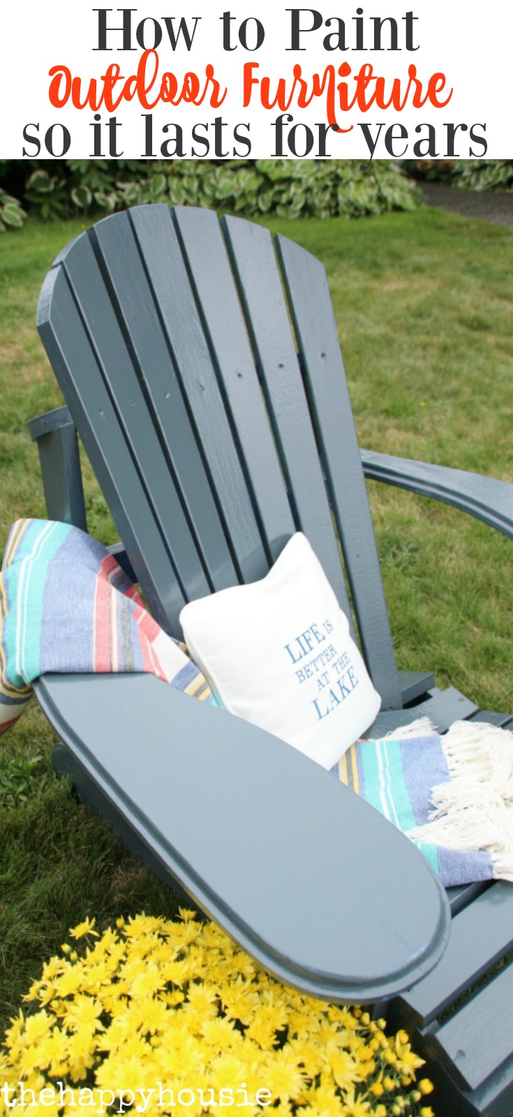 A large Adirondack chair on the grass with a pillow and blanket on it.