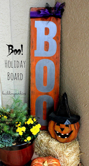 An outdoor sign that says BOO with a pumpkin in front of it on the front porch.