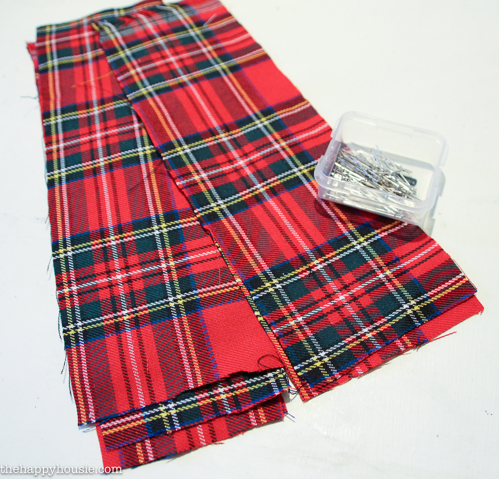The red plaid fabric laid out with some pins.
