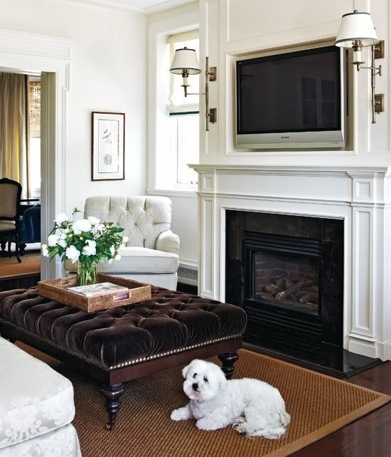 A white and black fireplace with a small white dog sitting in front of it.