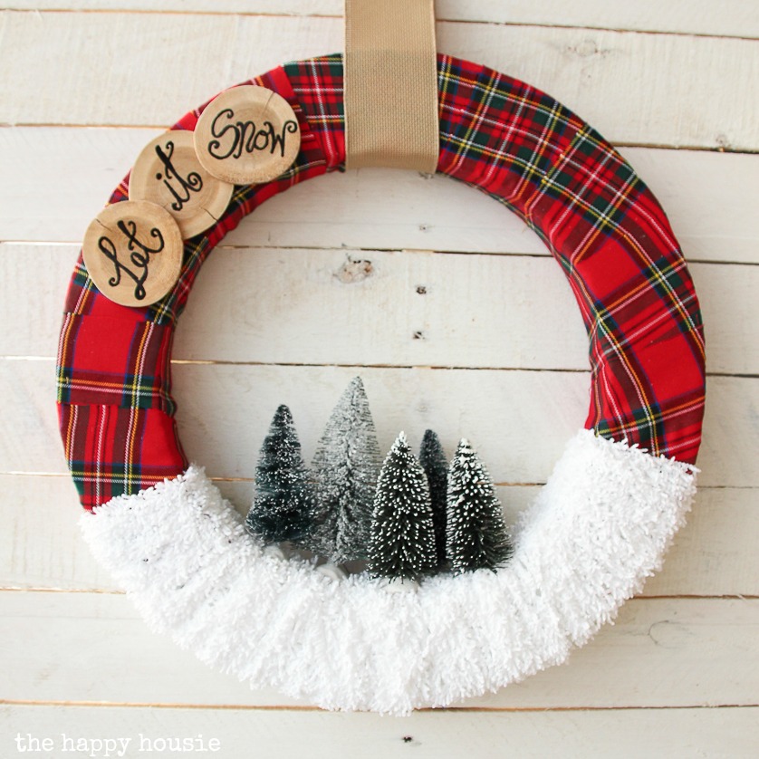 A red plaid wreath with little bottle brush trees and the words let it snow on it.