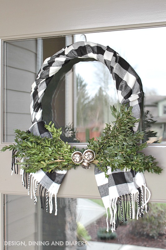 A buffalo checked wreath with fresh clippings and bells.
