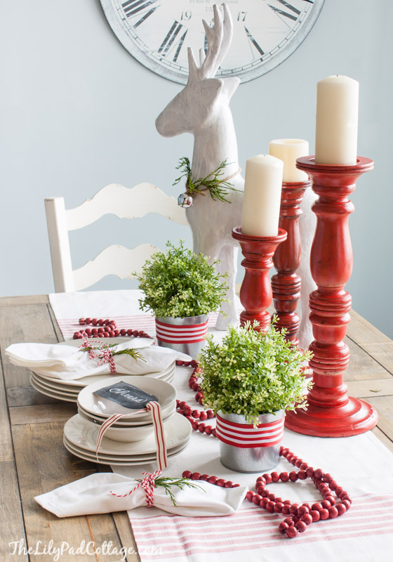 A dining room table with red candlesticks and red beads on it.