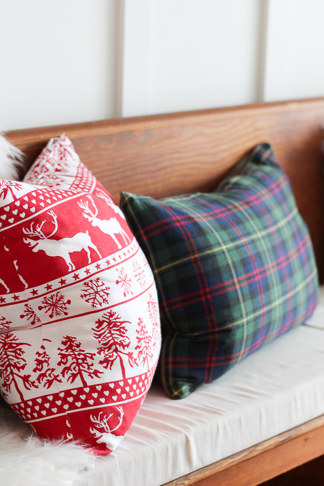 A red and white deer and tree pillow and a green plaid pillow.