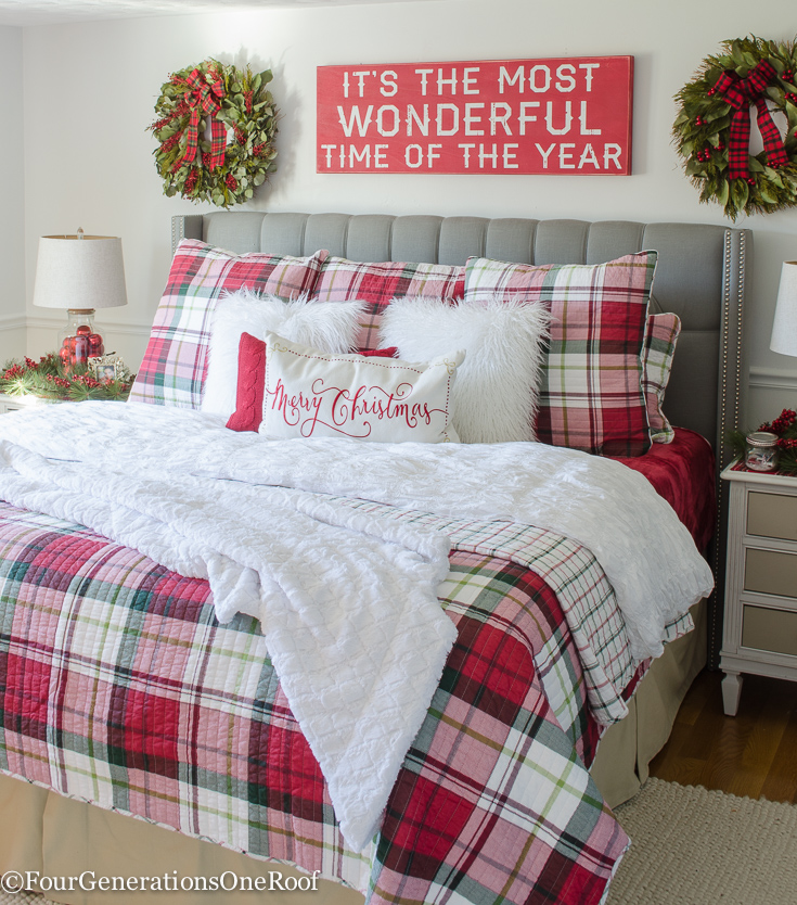 A bedroom with a red plaid bedspread and a Merry Christmas pillow on it.