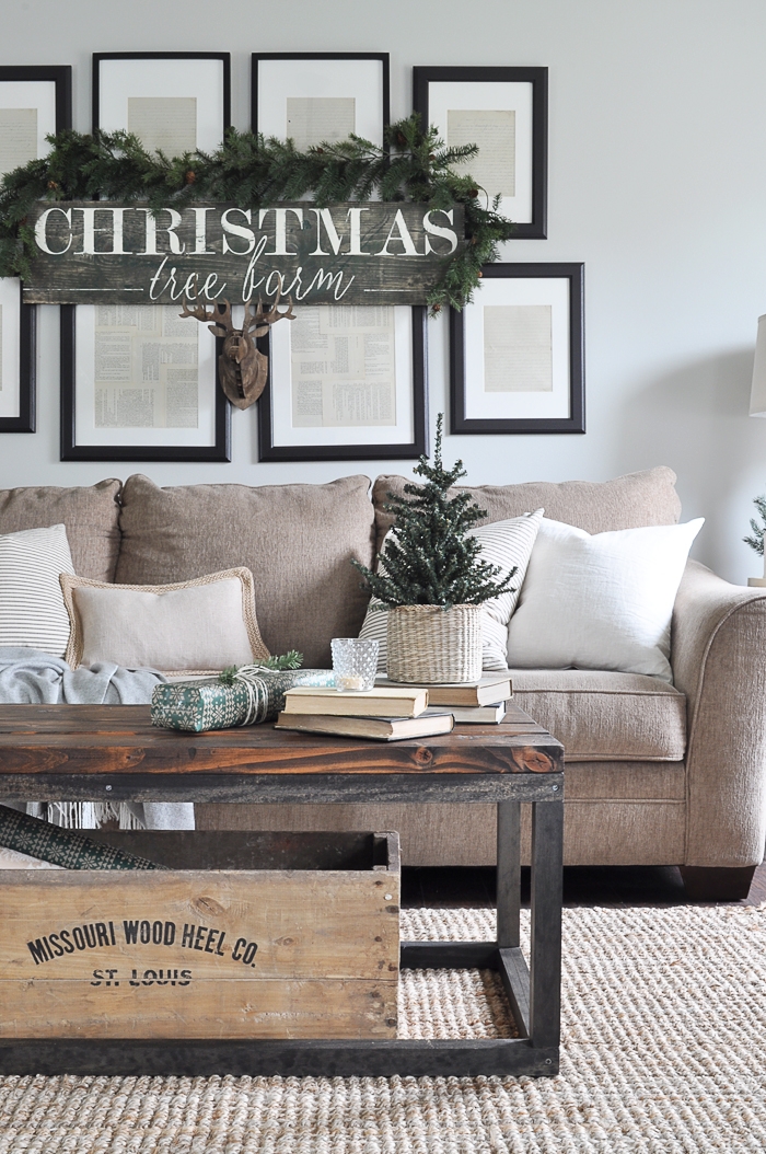 A neutral living room with a sign saying Christmas tree farm and a faux antlers underneath it.