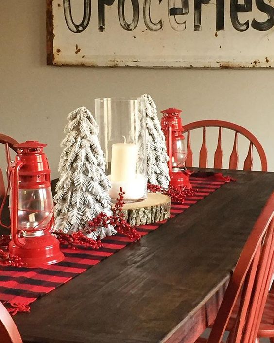 A wooden rustic dining room table with faux mini trees on it and red lanterns.