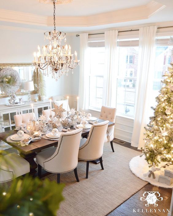 A large chandelier over the dining room table and a tree in the corner.