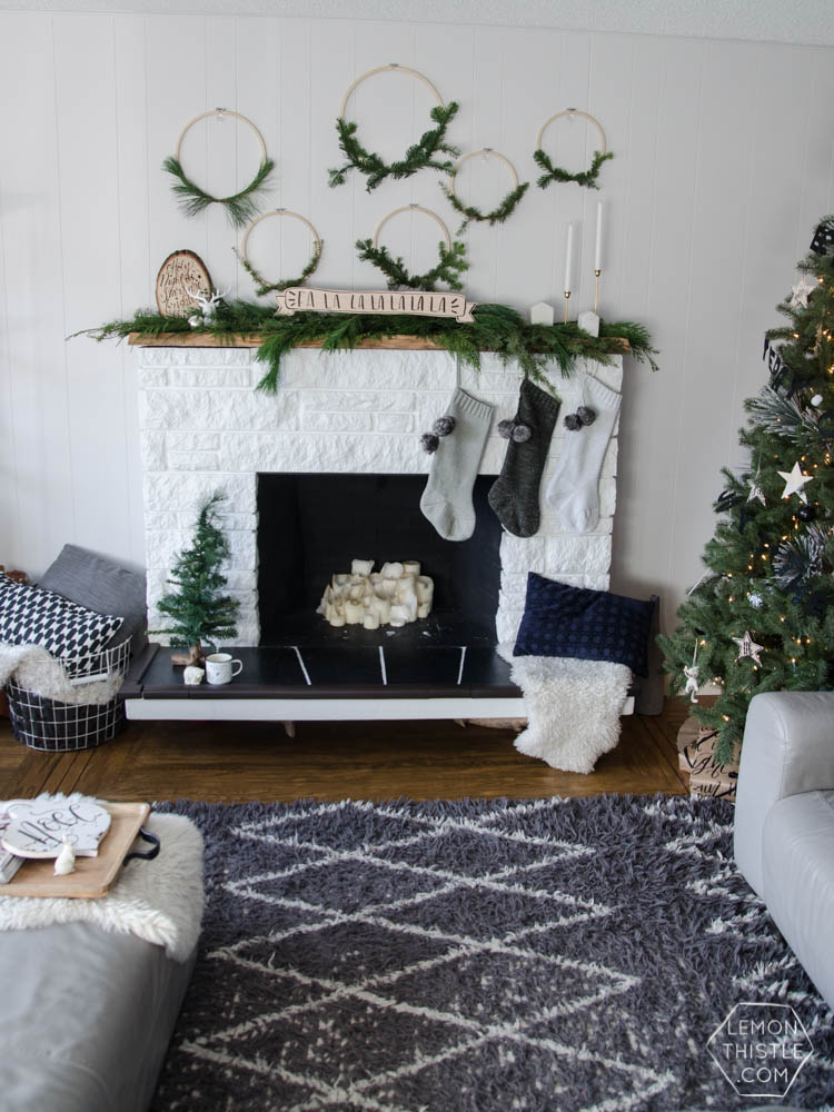 A white washed fireplace with mini wreaths and stockings hanging on it boho style.