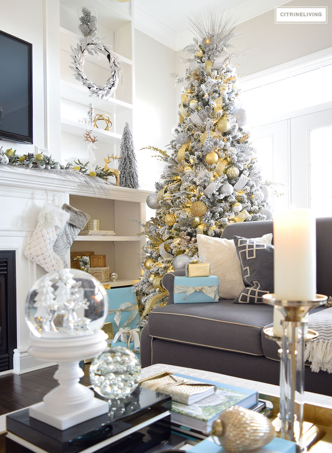 Grey couch, white fireplace and a flocked tree beside it.