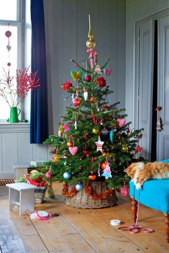 Christmas tree in the corner of a house with a cat lying beside it.
